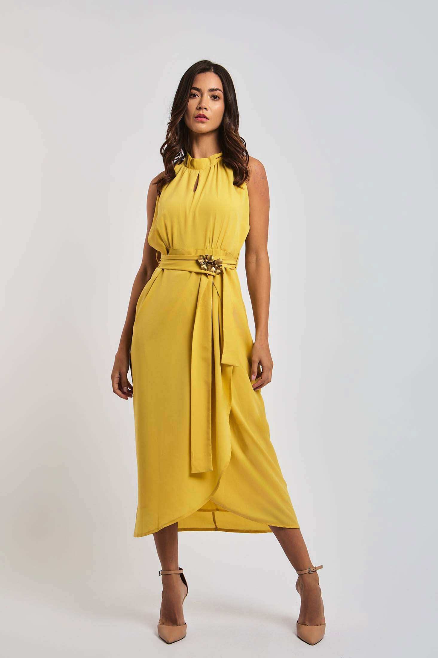 Woman in yellow sleeveless belted dress by Dalydress, standing against white background