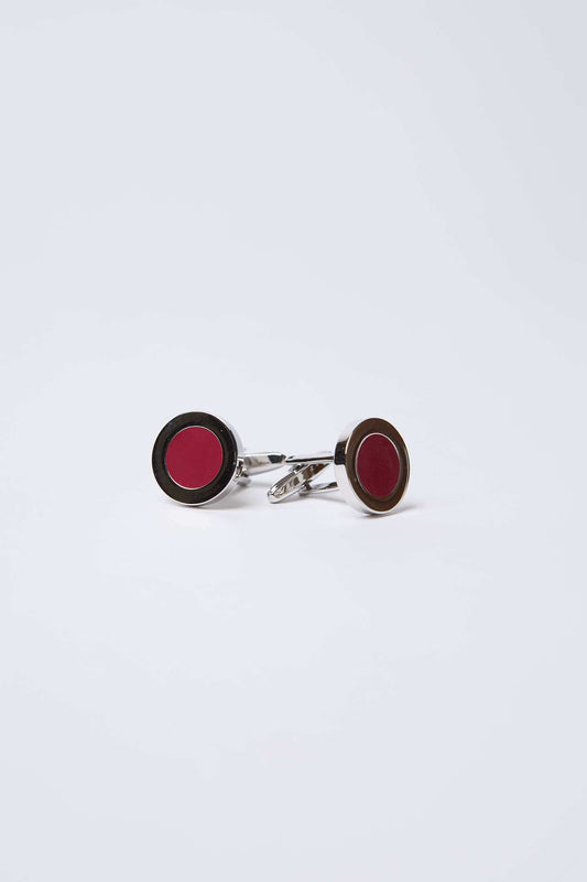Pair of round silver cufflinks with red enamel center on a white background