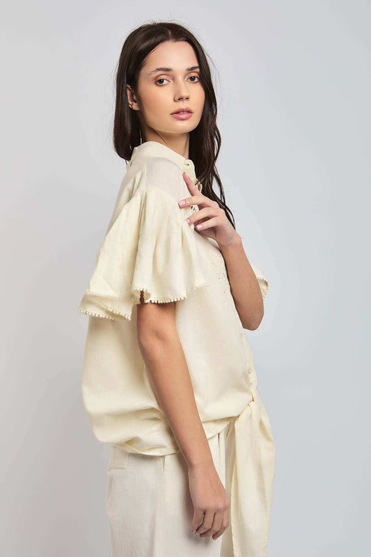 Woman wearing cream short sleeve blouse with ruffled sleeves and matching pants