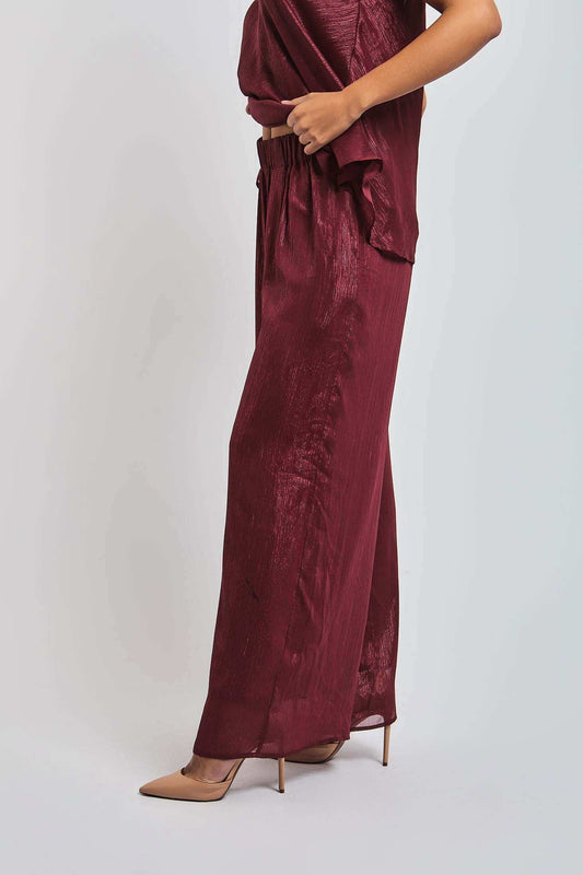 Woman wearing burgundy wide-leg satin pants and matching top with nude heels