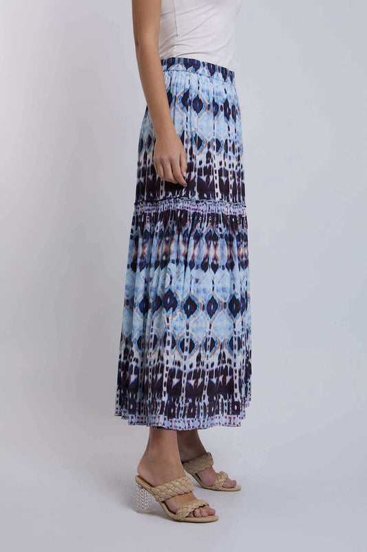 Woman wearing blue and black patterned maxi skirt with white sleeveless top and braided sandals