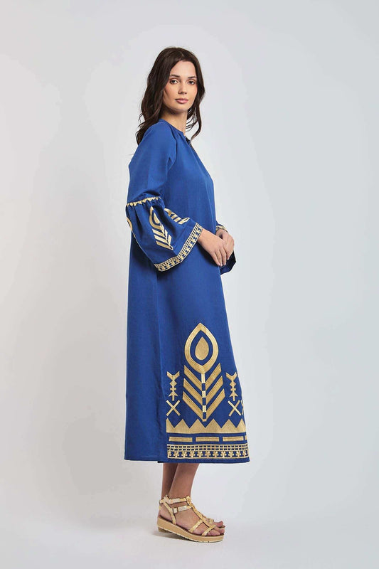 Woman wearing a blue dress with gold geometric patterns and flared sleeves, standing sideways