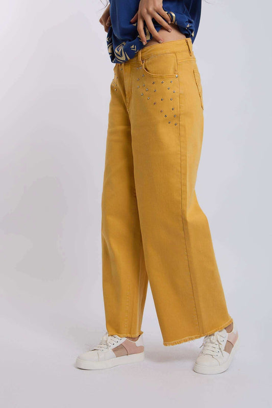 Woman wearing yellow wide leg jeans with silver studs, casual sneakers, and a blue top
