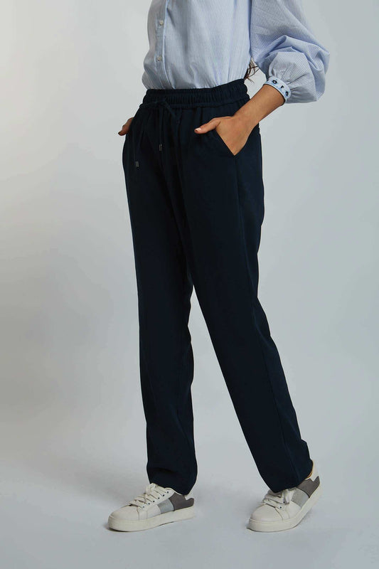Women's casual navy jogger pants with elastic waistband and drawstring, styled with white sneakers and a light blue button-up shirt.