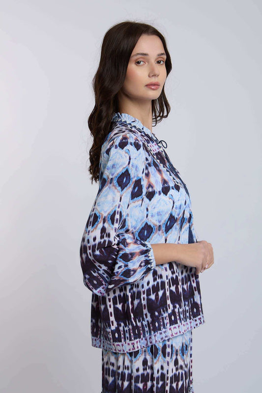 Woman wearing a blue and purple patterned blouse with long sleeves, side view