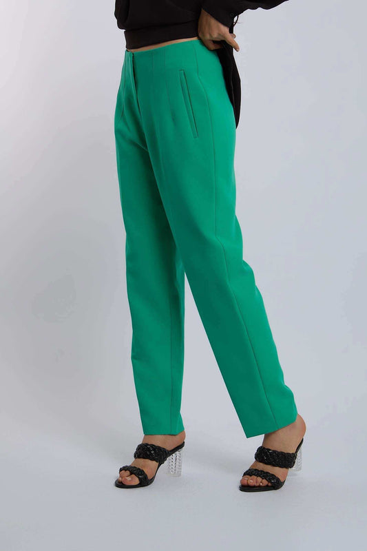 Woman wearing bright green tailored pants and black heeled sandals on white background