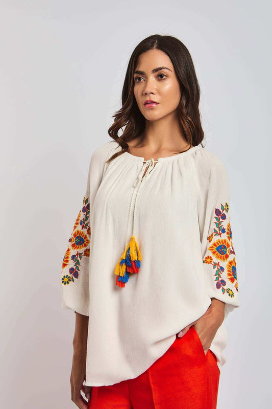 Woman wearing white embroidered peasant blouse with tassels and orange pants