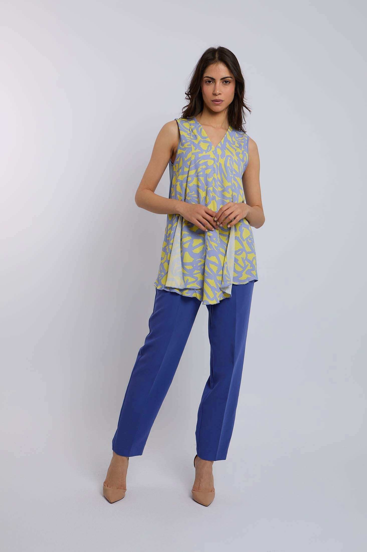 Woman wearing a sleeveless yellow and blue patterned top with blue pants and beige heels