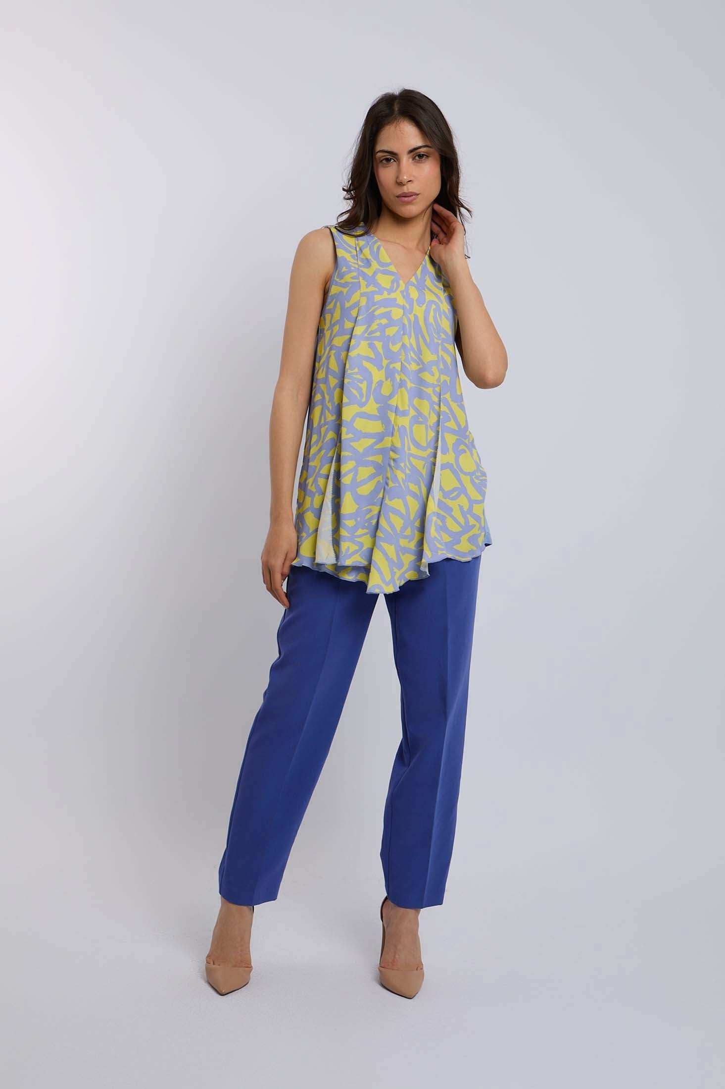 Woman wearing a sleeveless yellow and blue patterned top with blue pants and beige heels