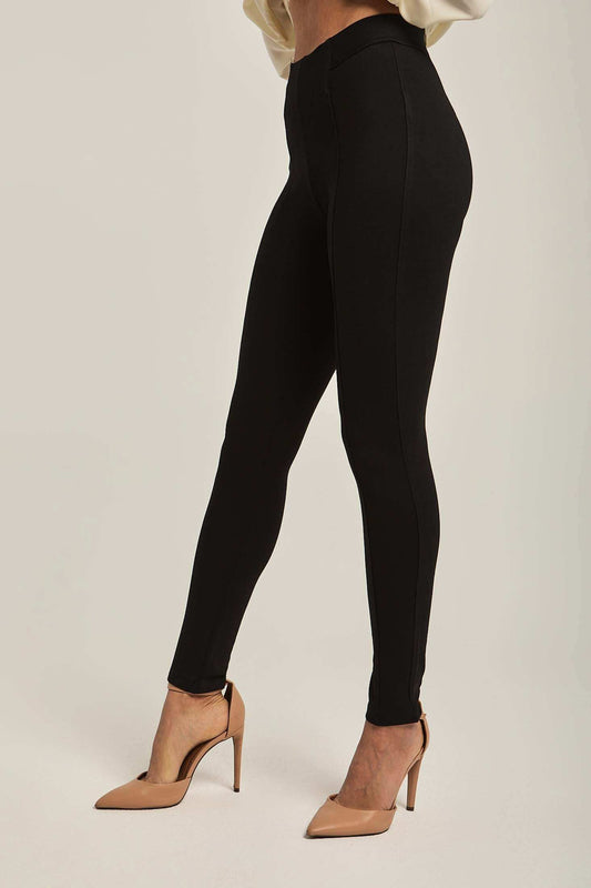 Women's high-waisted black skinny pants styled with beige heels on a neutral background