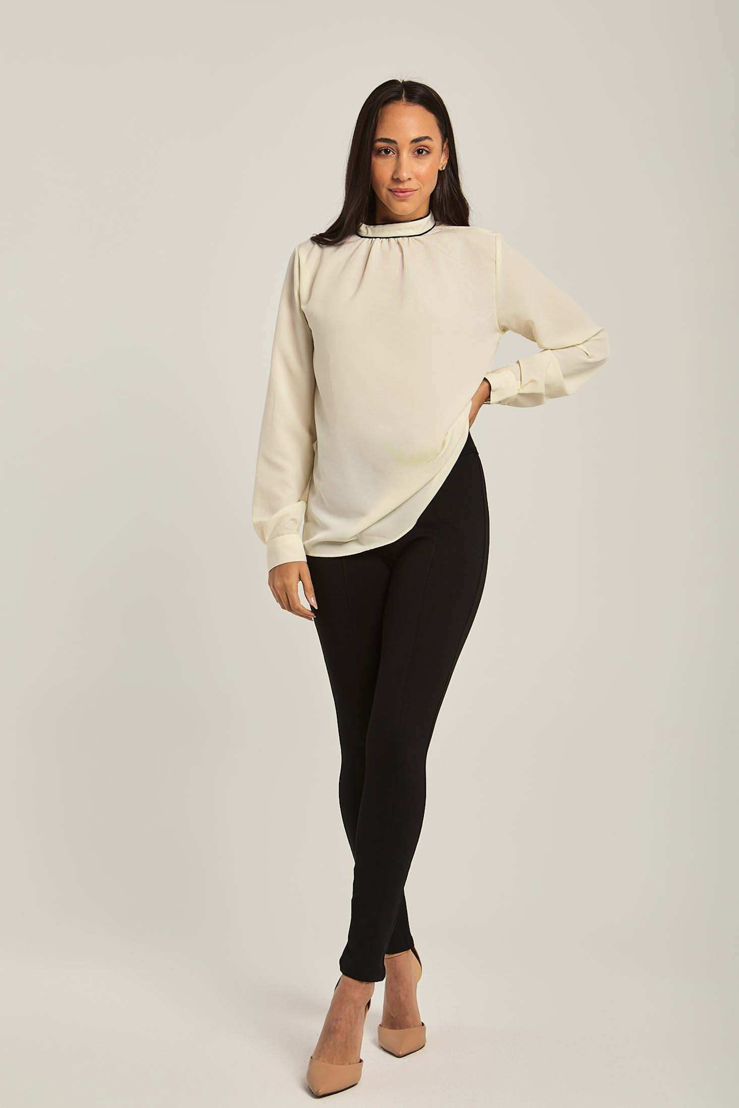 Woman modeling an off-white long sleeve blouse with black skinny pants and beige heels